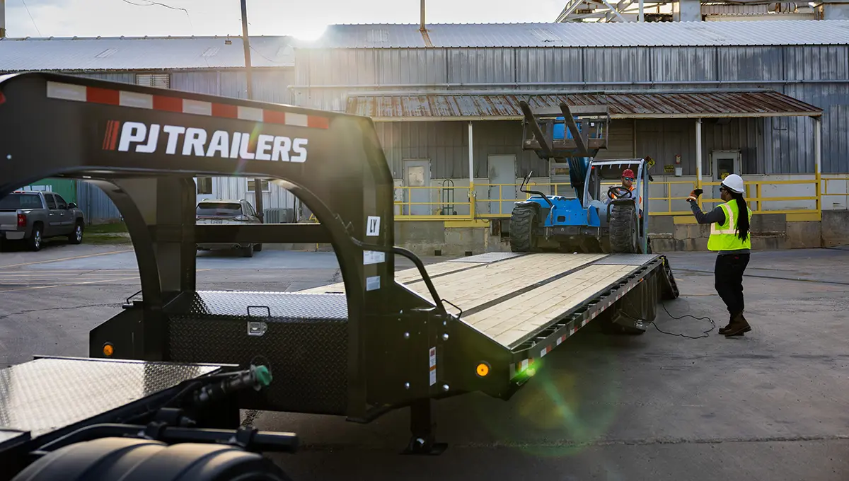 Workers loading a forklift onto the Low-Pro With Hydraulic Dove Trailer